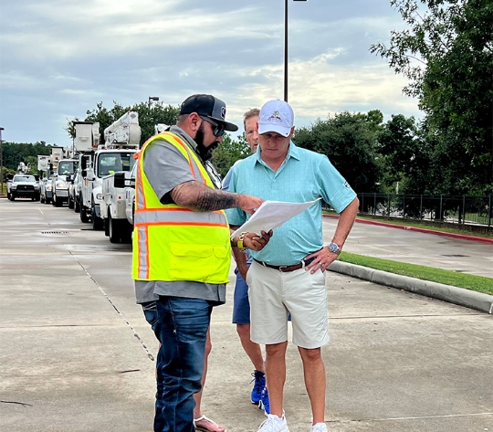 A man in a yellow visibility vest shows Brad Bailey documents. They are standing in front of bucket trucks.